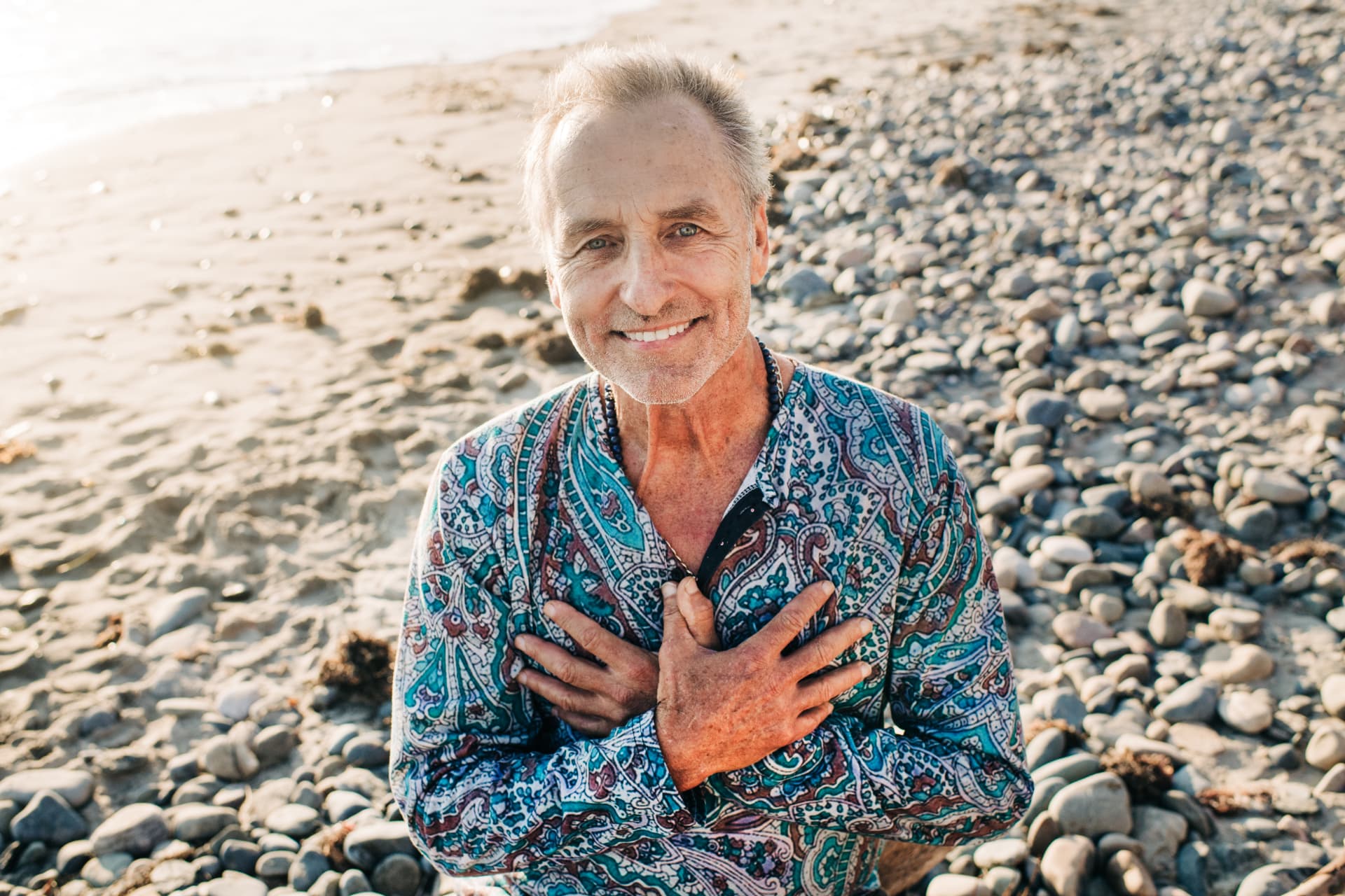 Loni Tydon smiling on a pebble beach with hands over his heart