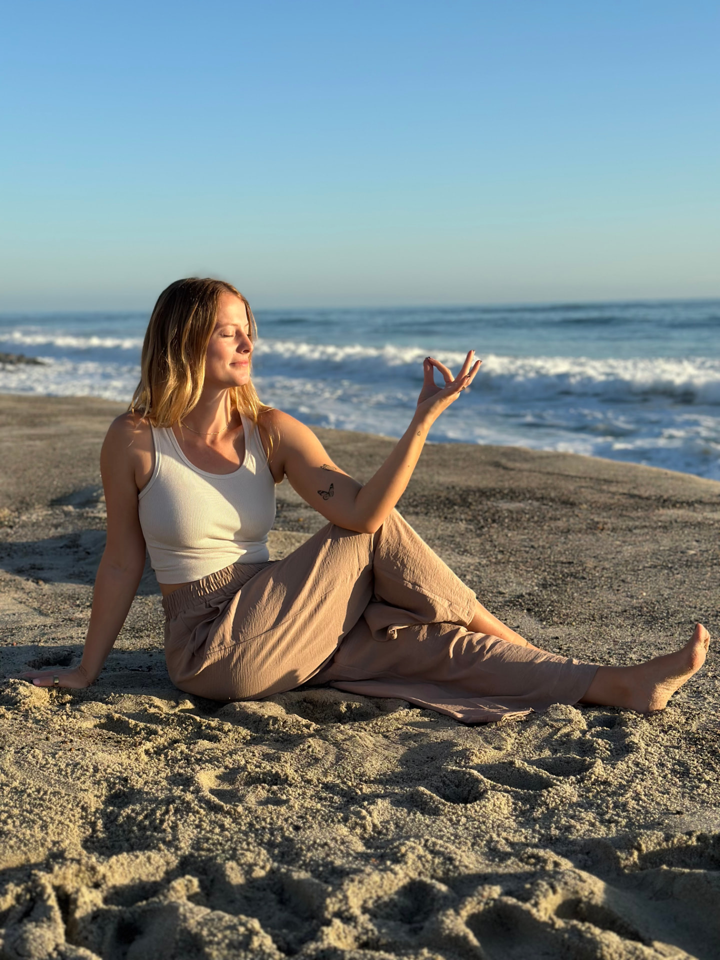 Ellie Morgan seated on the beach in a meditative pose at golden hour