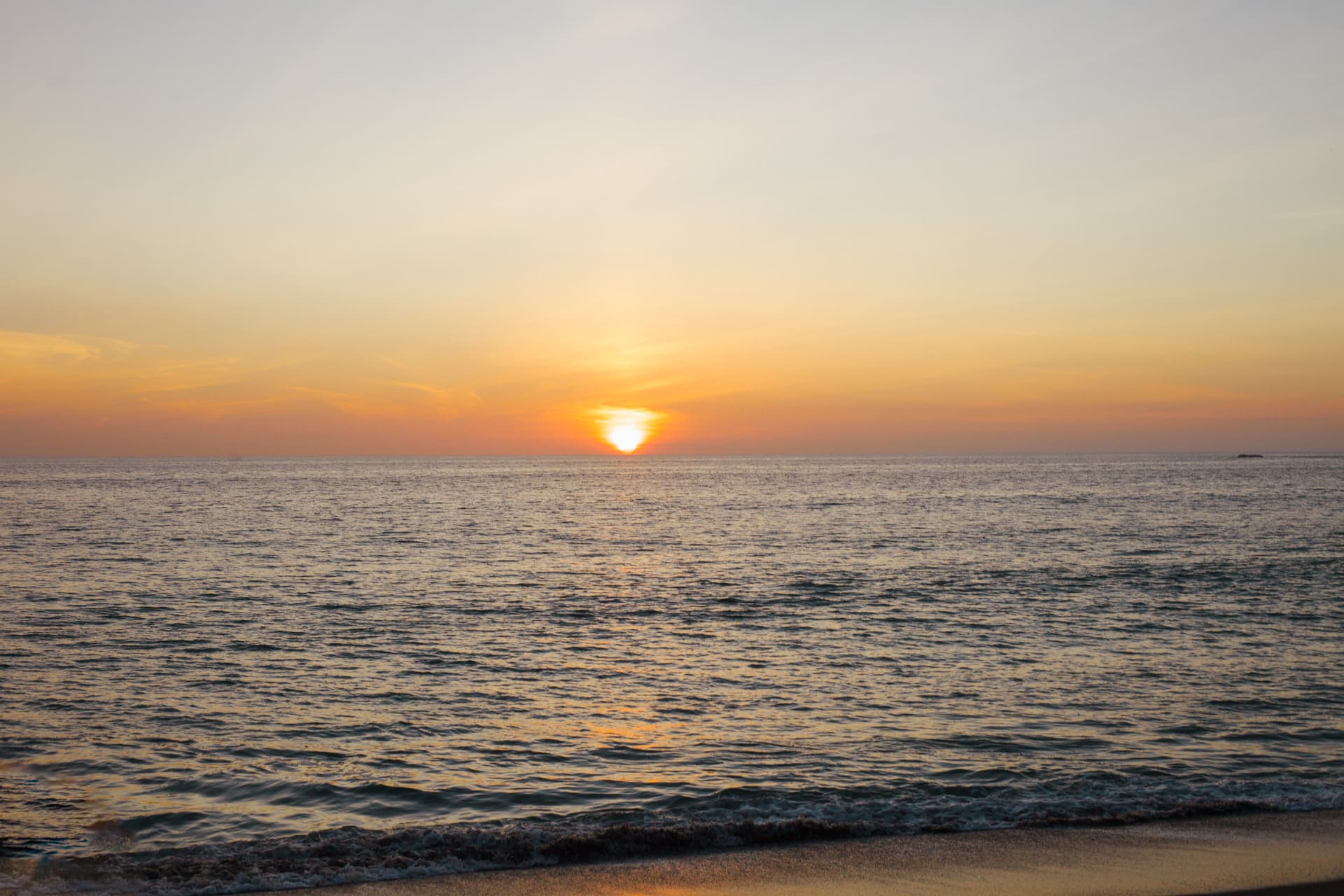 A peaceful sunset over a calm ocean with gentle waves lapping onto a sandy beach