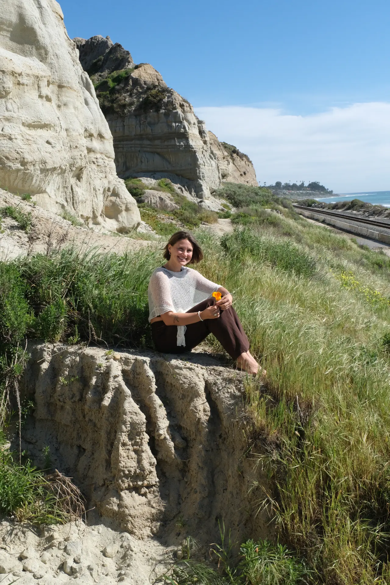 Brie Bush sitting on a coastal cliff above the beach