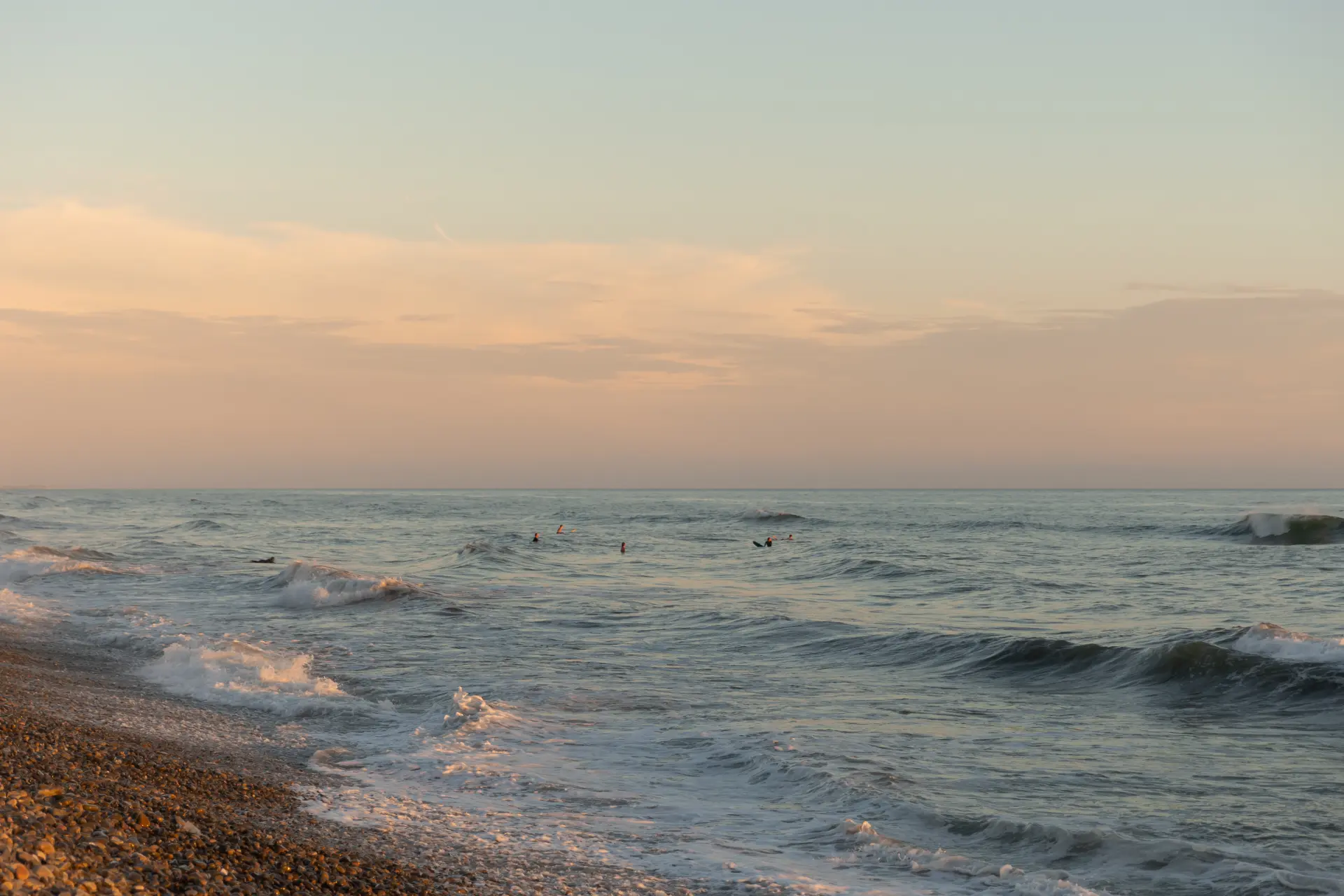 Surfers in the ocean off a pebble beach on the San Clemente shoreline at dusk