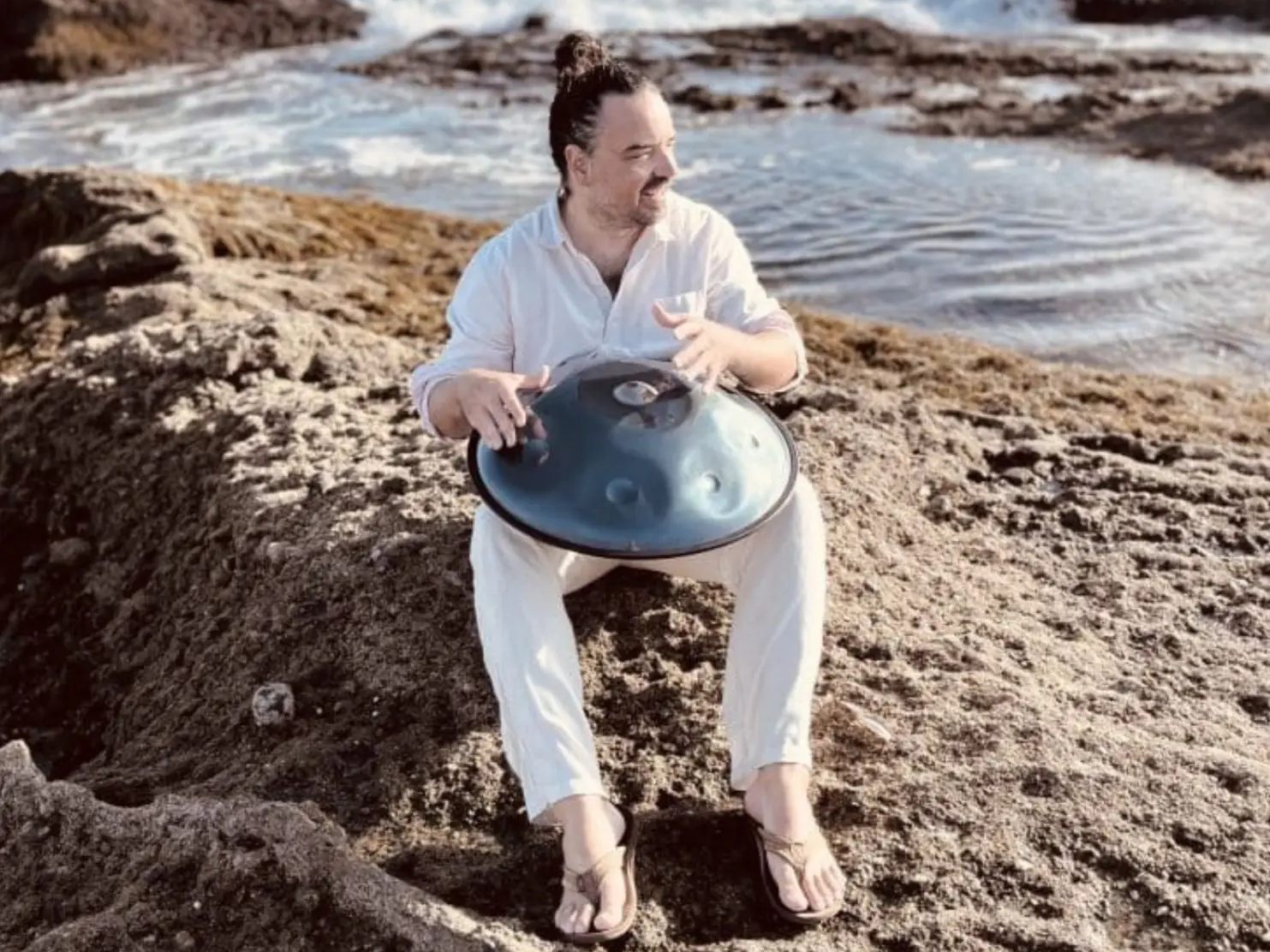 Lindsey Miller seated on a rock holding a handpan in a slot canyon