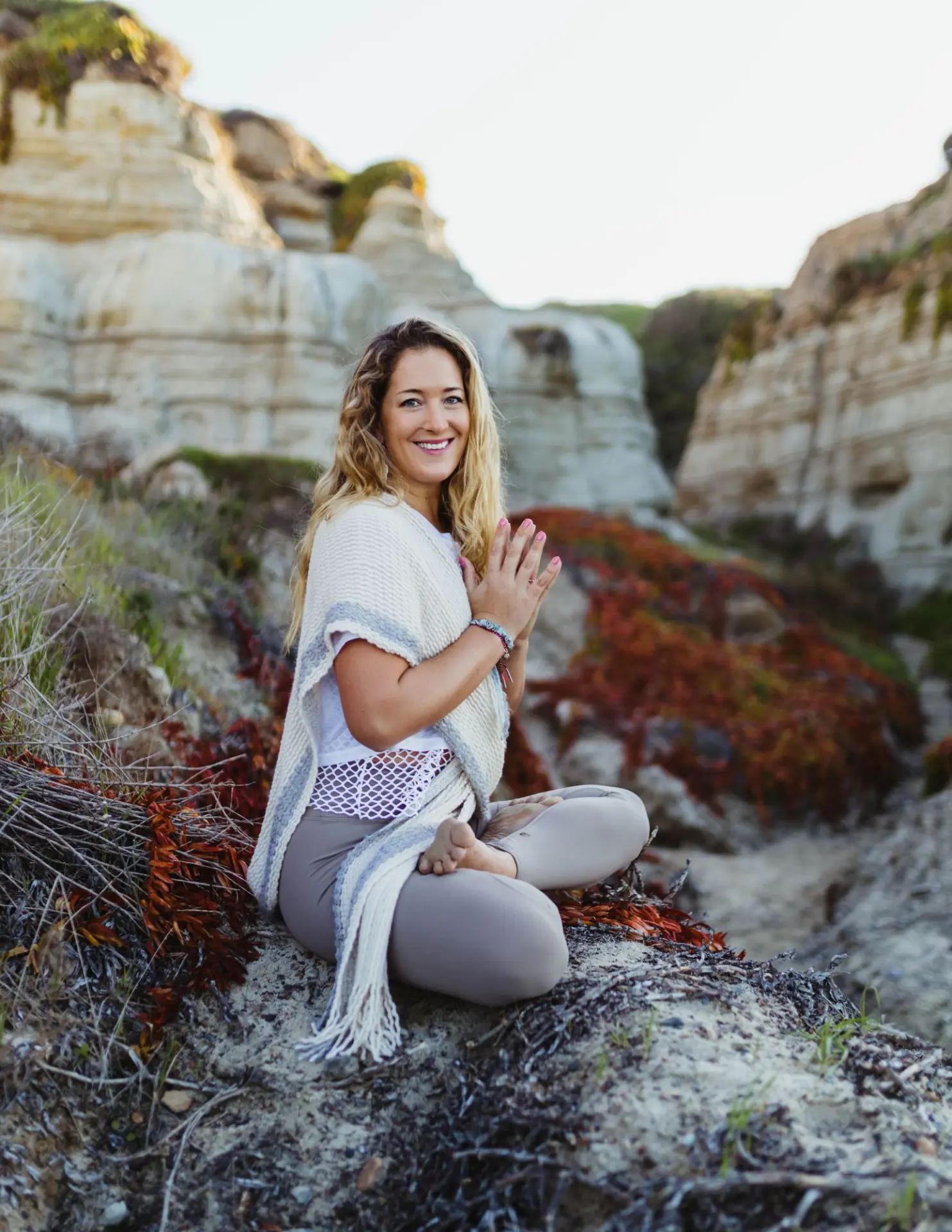 Chloe Porter-Gentile seated in a meditative pose with hands pressed together on a coastal cliff